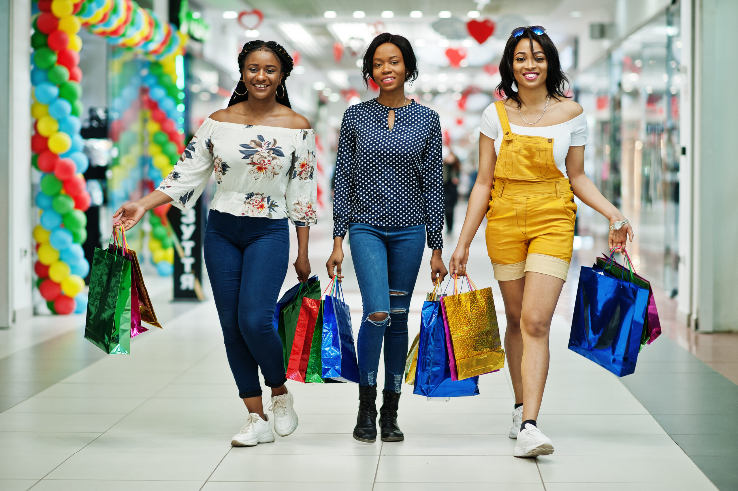 Beautiful three well-dressed afro american girls with colored shopping bags walking in mall.